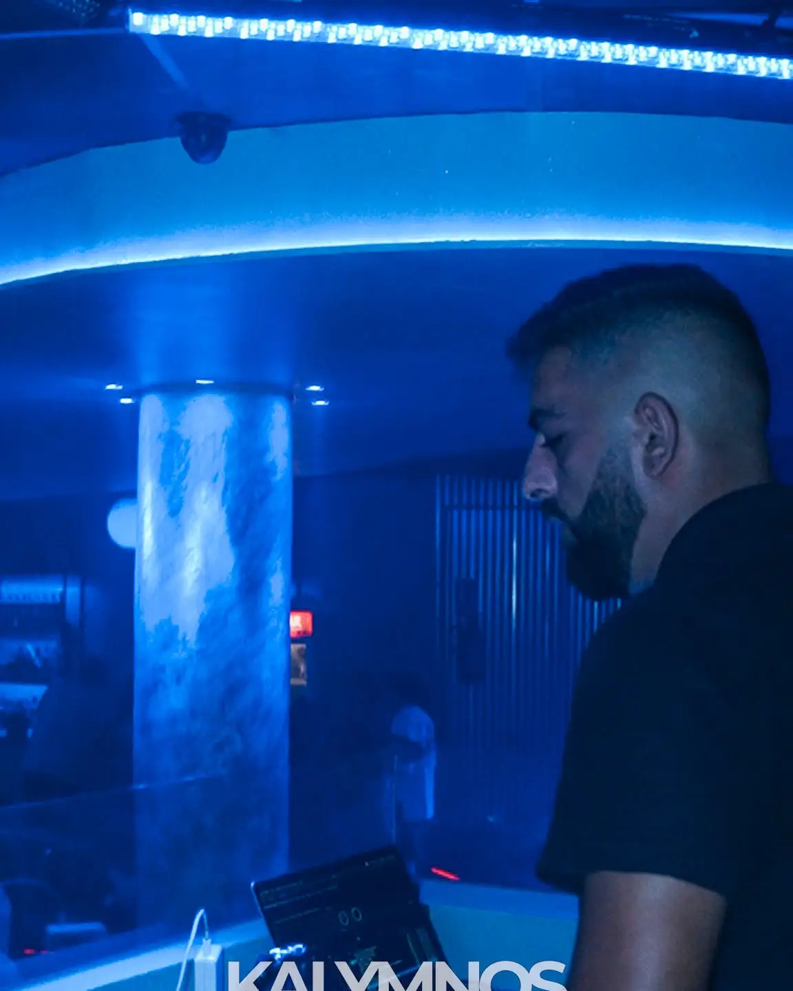 DJ nella consolle del Kalymnos, con la colonna e il soffitto illuminati di blu